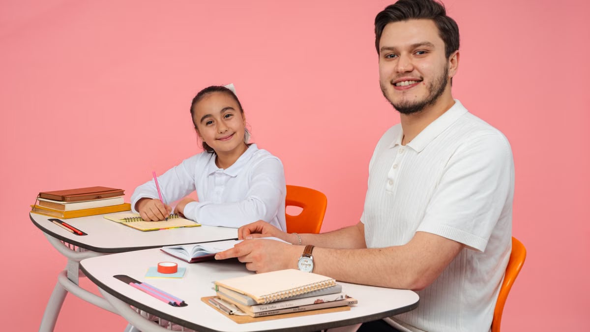 Teacher and student smiling in a classroom setup with bright pink background.